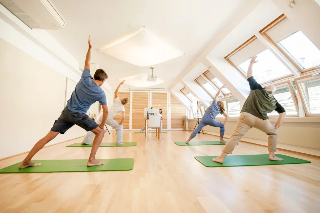 Yoga-Kurs im Seminarraum Berg7 Wien – Gruppe bei Krieger-Pose auf grünen Matten